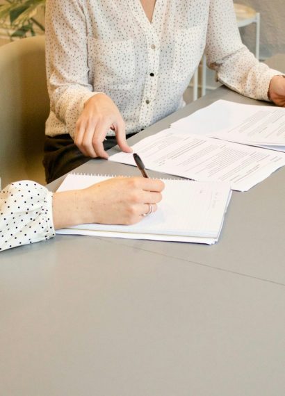 woman signing on white printer paper beside woman about to touch the documents