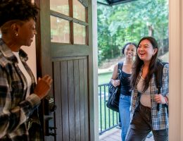 Two women arriving at a doorway, greeted by another woman.
