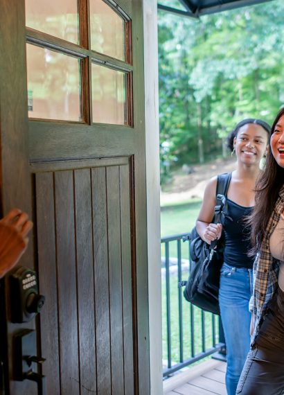 Two women arriving at a doorway, greeted by another woman.