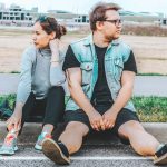 woman looking at her right sitting at curb beside man looking at his left