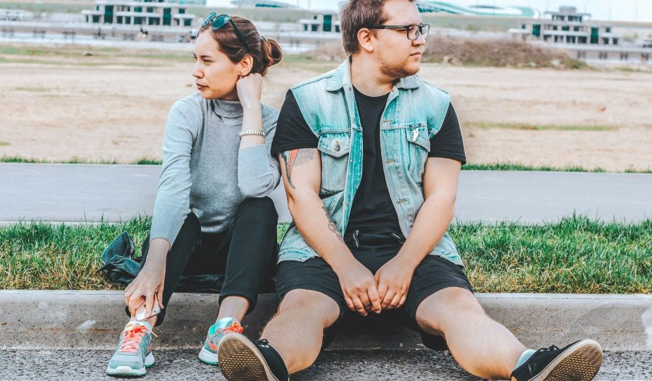 woman looking at her right sitting at curb beside man looking at his left